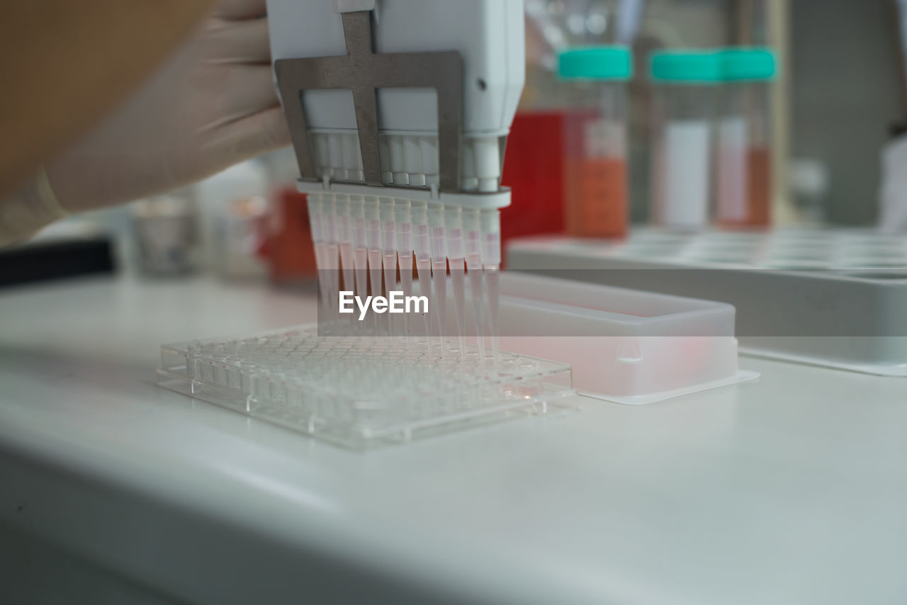 Cropped hands of biologist holding pcr device while pouring liquid in plastic container at laboratory