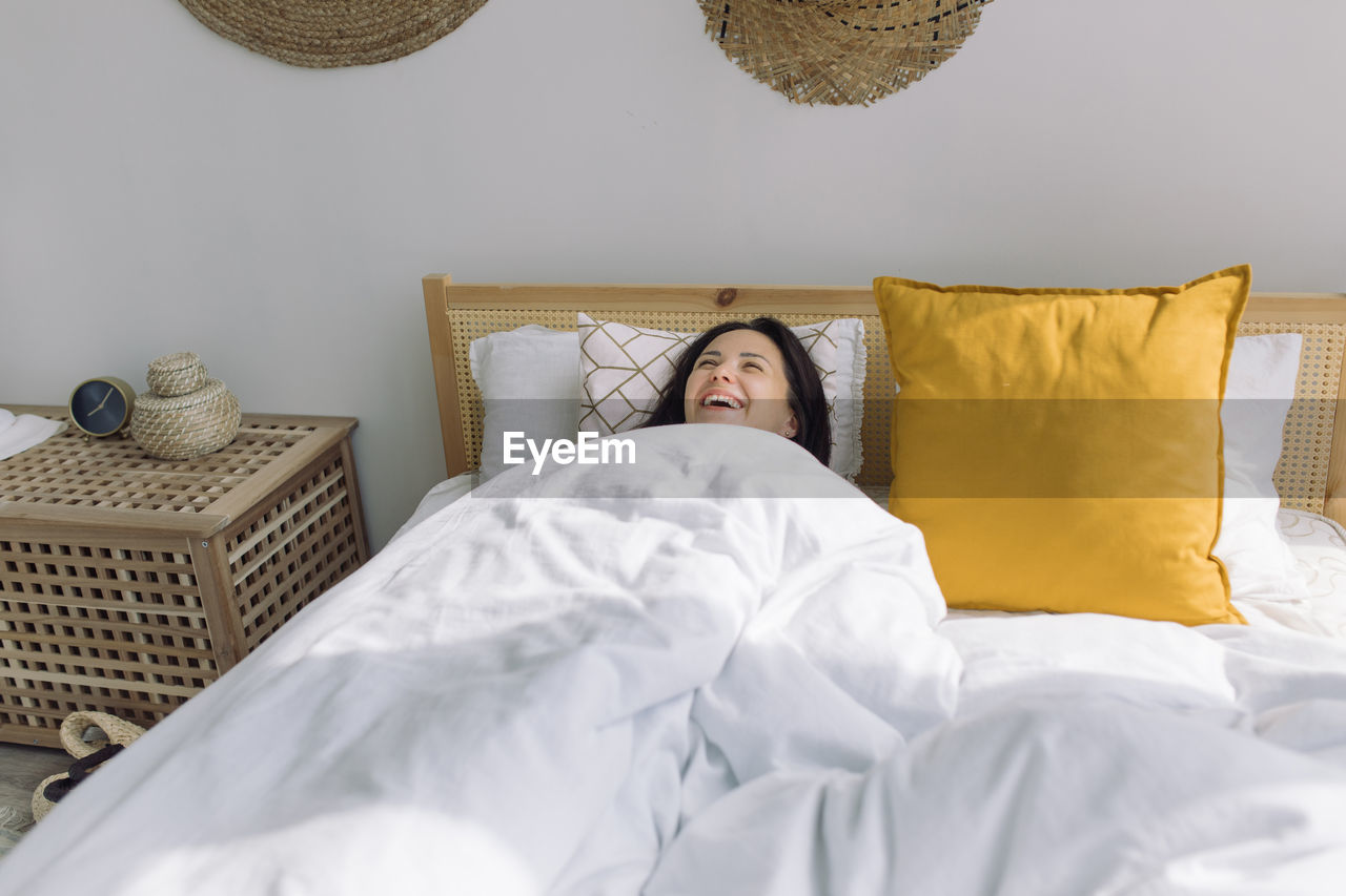 High angle view of woman laughing while sleeping on bed