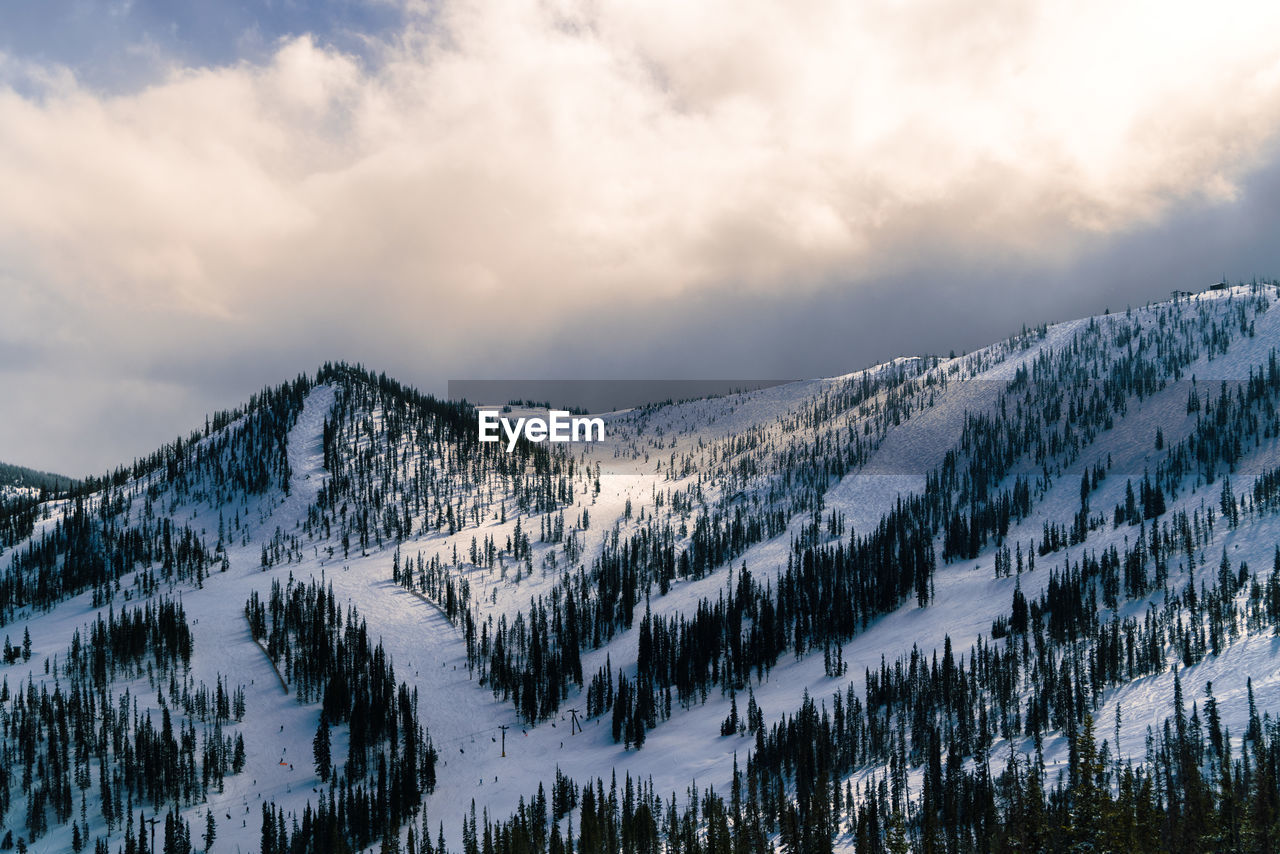 Scenic view of snowcapped mountains against sky with skiers