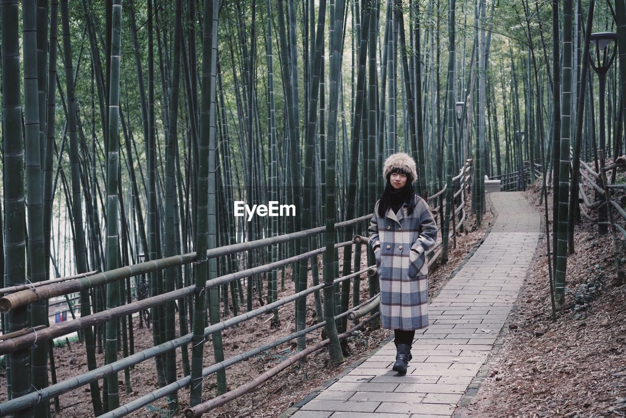 Full length of woman wearing warm clothing standing on footpath at forest
