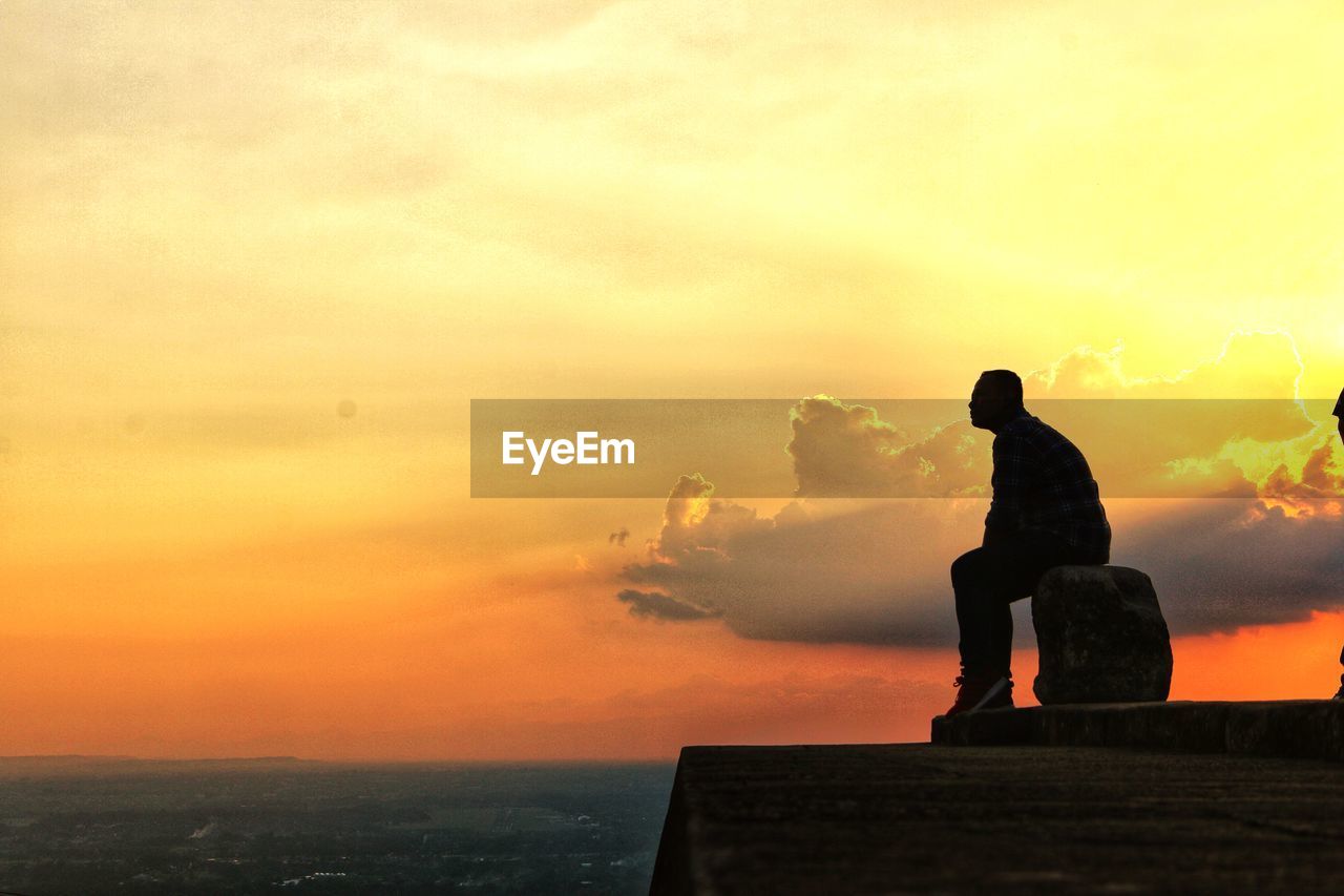 Silhouette man sitting against orange sky