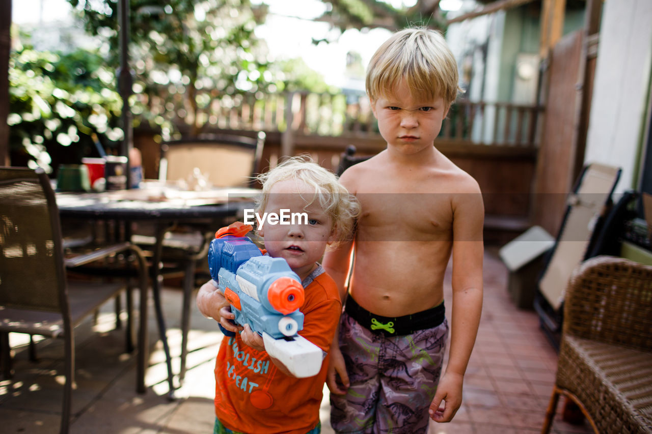 Brothers posing for camera in front yard holding water gun