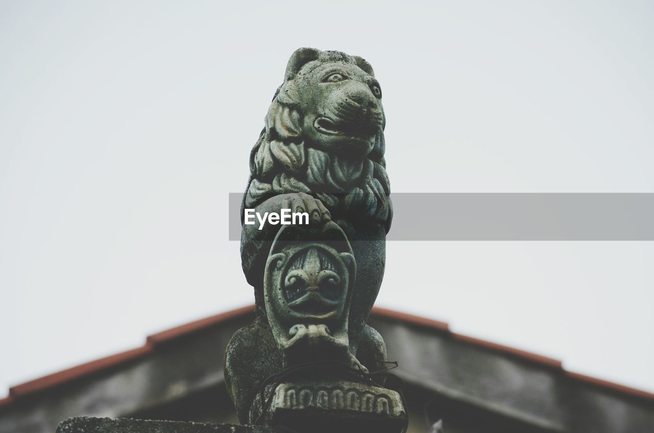 Low angle view of lion sculpture by building against clear sky