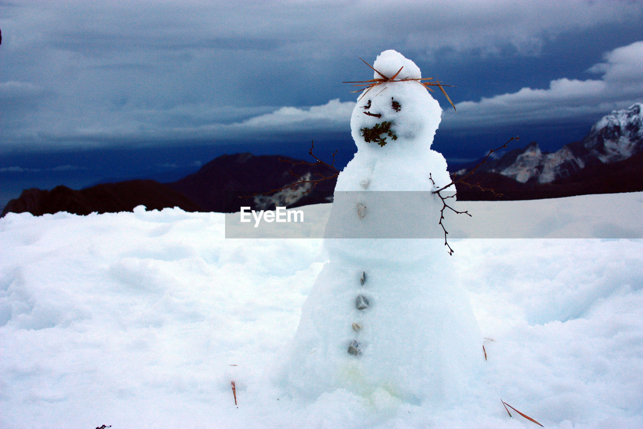 White snowman with twigs and stones and the panorama of apuan alps between mountains and blue sea