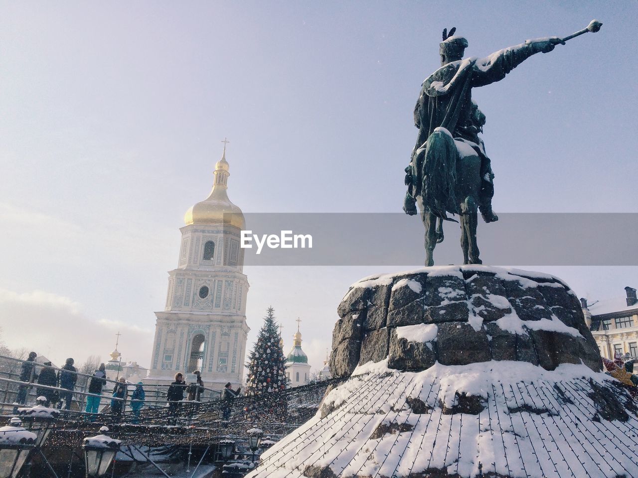 People looking at snow covered statue against church during christmas