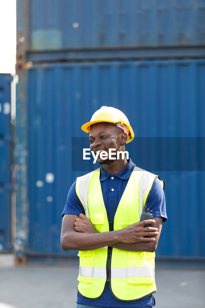 MAN WORKING WITH ARMS RAISED STANDING AGAINST SKY