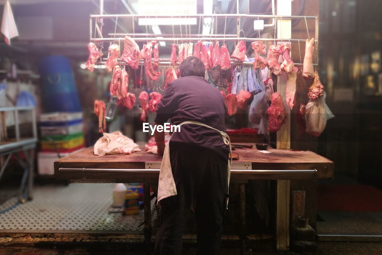 Rear view of butcher with fresh meat in shop