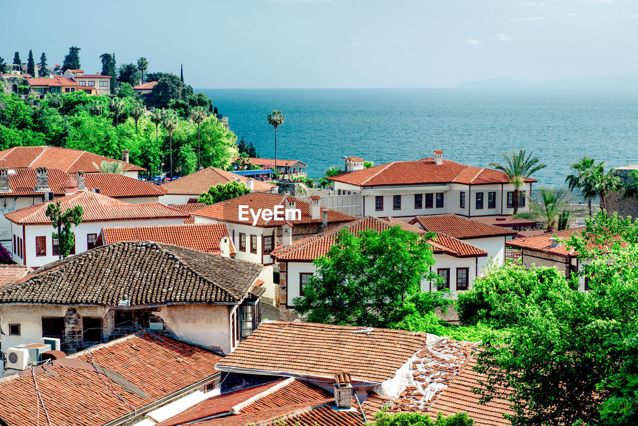 Houses and trees by sea against sky