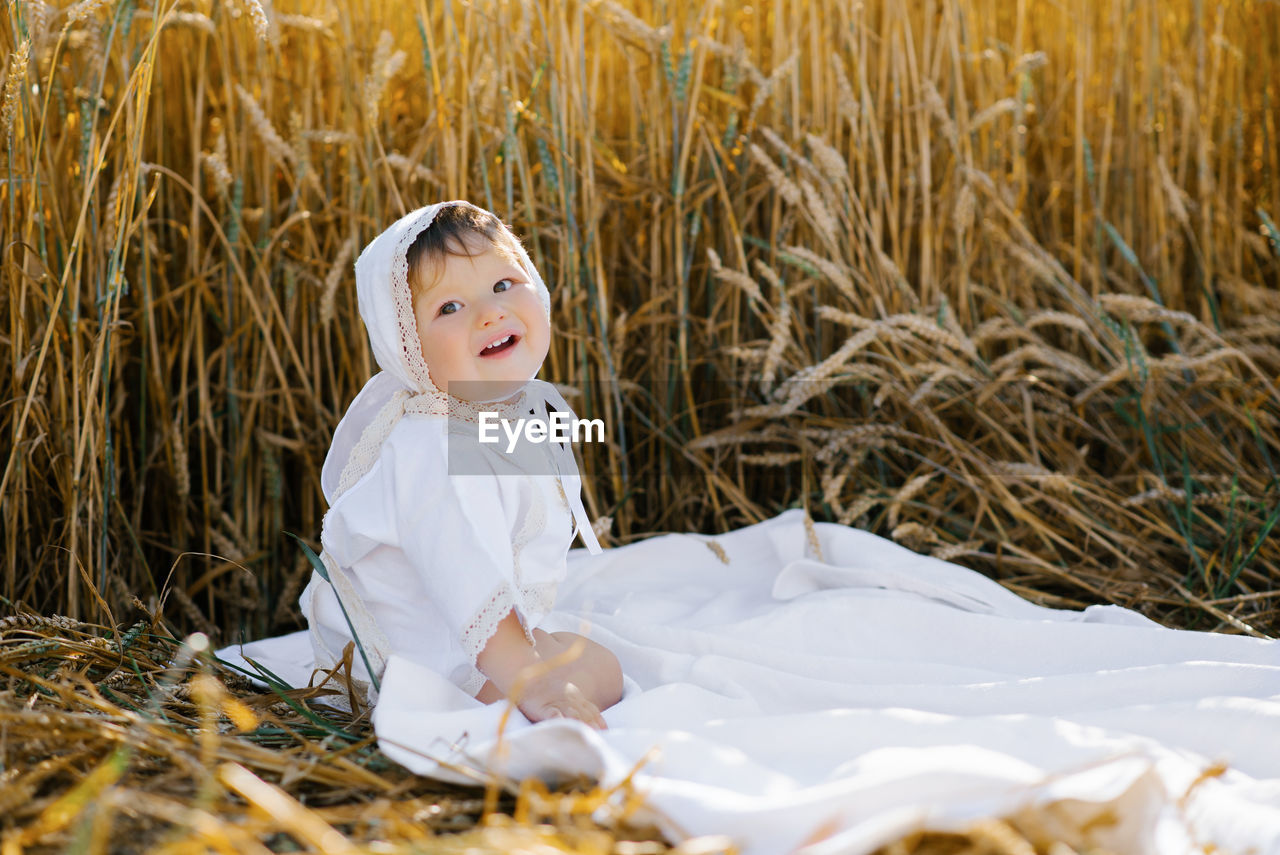 Sweet eight-month-old baby boy sitting on a blanket in a field and laughing