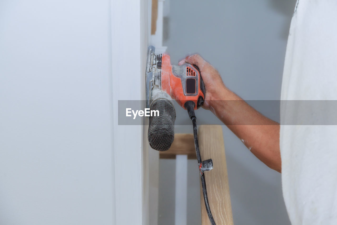 Midsection of man holding sander on wall