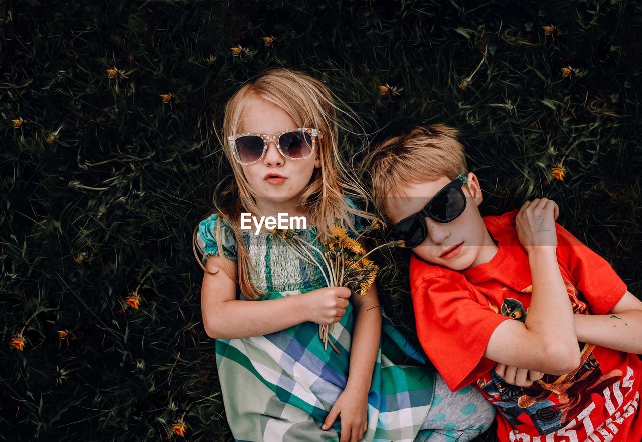 High angle portrait of girl and boy wearing sunglasses while lying on grass