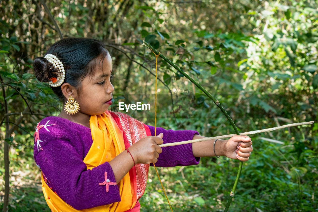 An indigenous indian teenage girl is practicing alone archery in the jungle with a bow and arrow. 