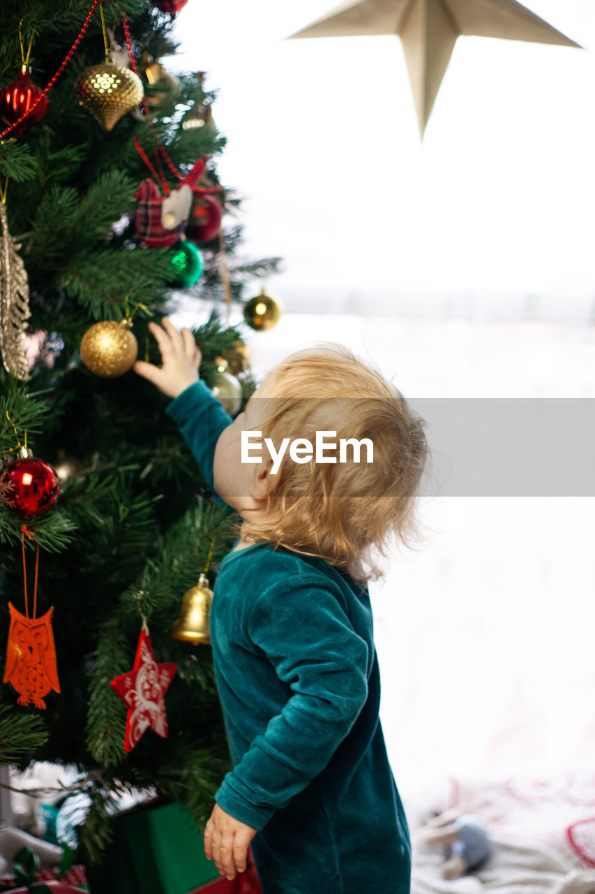 Cute little kid looks at christmas tree decorated with toys and garland. new year and christmas.