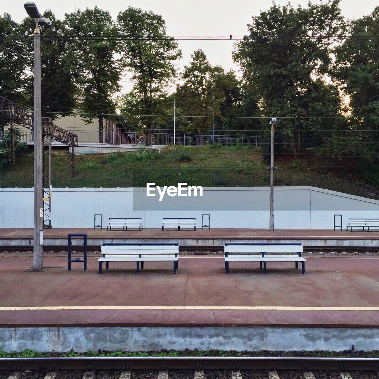 Empty benches at railroad station platform by trees against sky