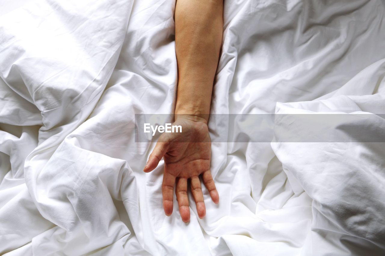 Cropped image of man hand on crumpled blanket at bed