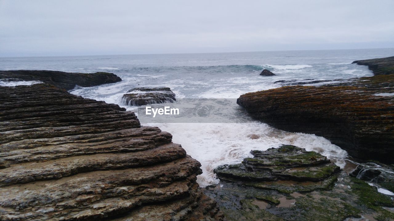 Scenic view of rocky coastline against cloudy sky