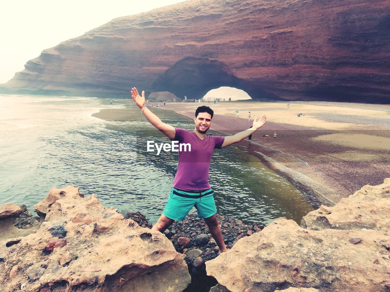 FULL LENGTH OF YOUNG MAN STANDING ON ROCK AT SEA