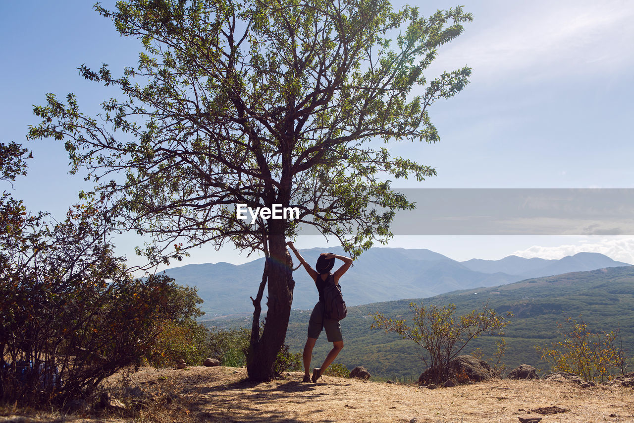 Woman in a hat stands by a tree on a mountain in the summer in the crimea