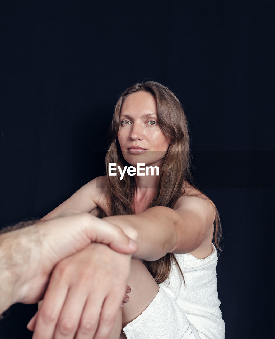 Attractive woman giving hand to man on black background. support, looking into camera, long hair.