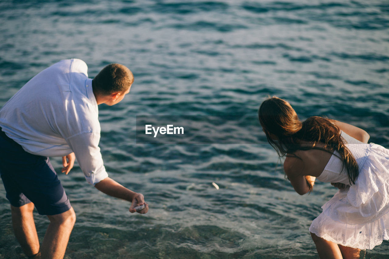 Rear view of couple skimming stones in lake