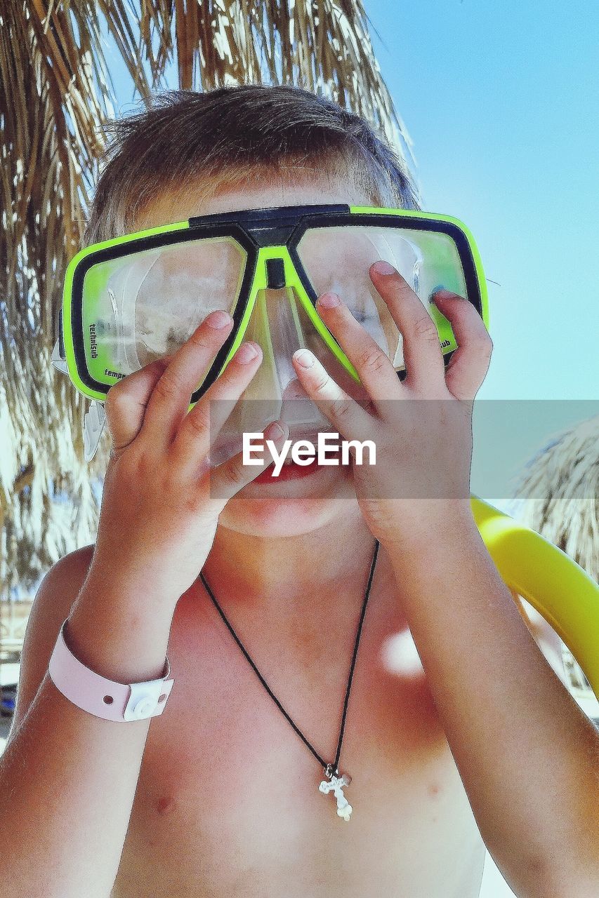 CLOSE-UP PORTRAIT OF WOMAN HOLDING SUNGLASSES AGAINST BLURRED BACKGROUND