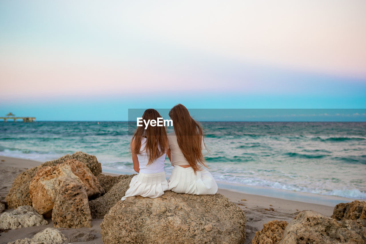 rear view of woman standing at beach against sky during sunset