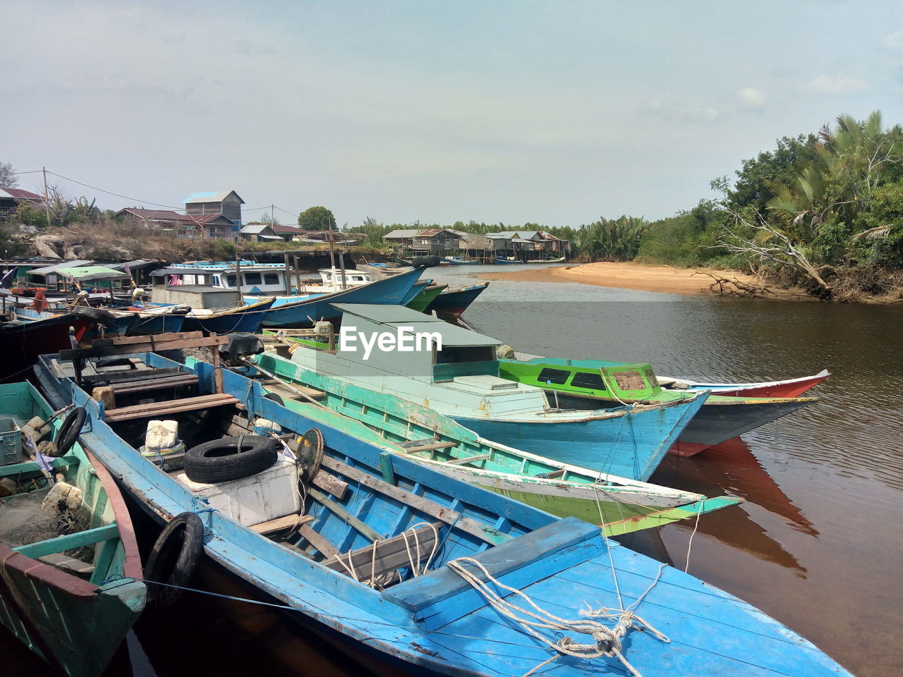 Boats moored on river by trees against sky