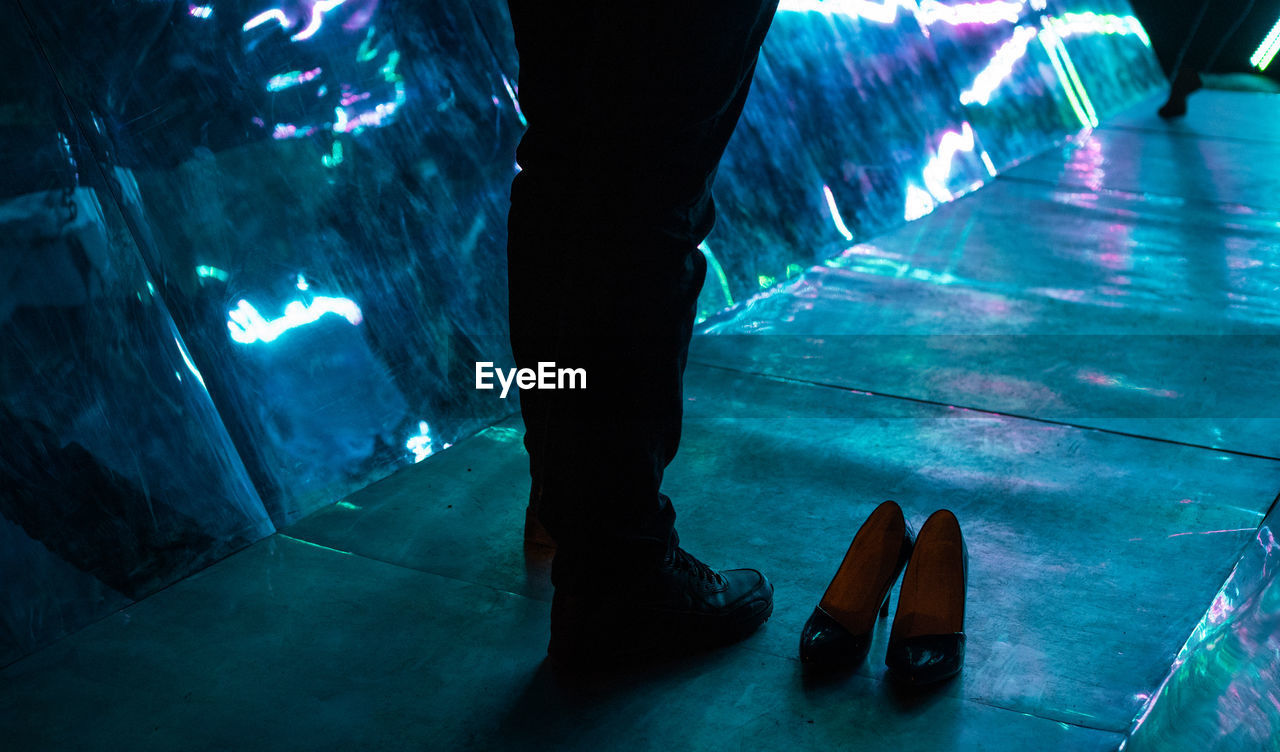 Low section of man standing on footpath at night