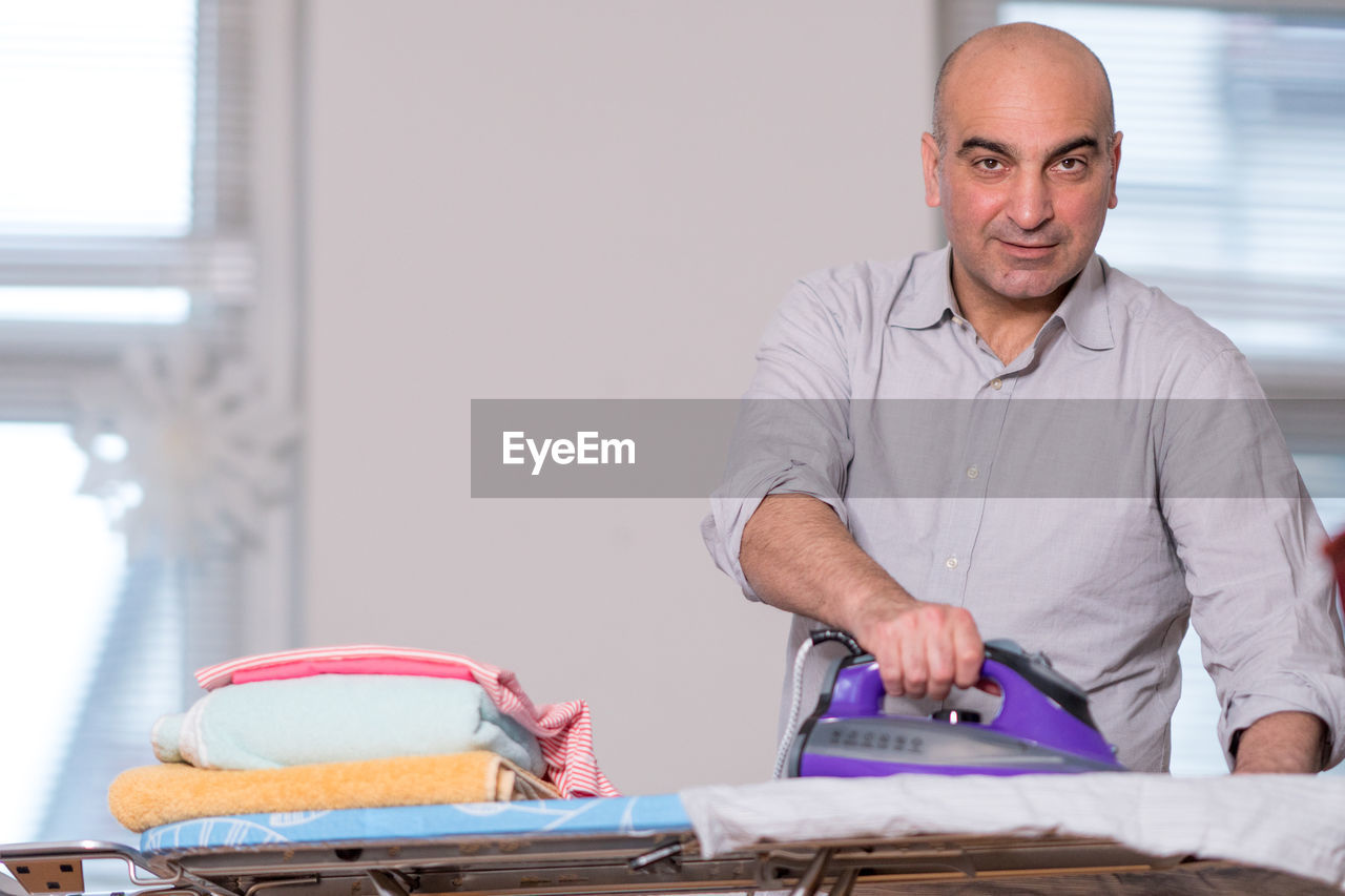 Portrait of man ironing clothes at home