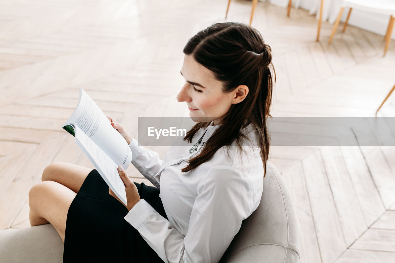 High angle view of woman reading book sitting on sofa