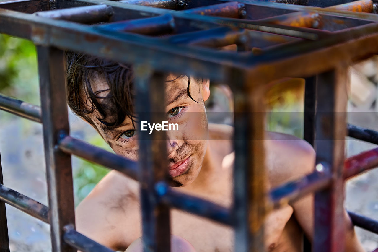 Portrait of boy looking through metal grate