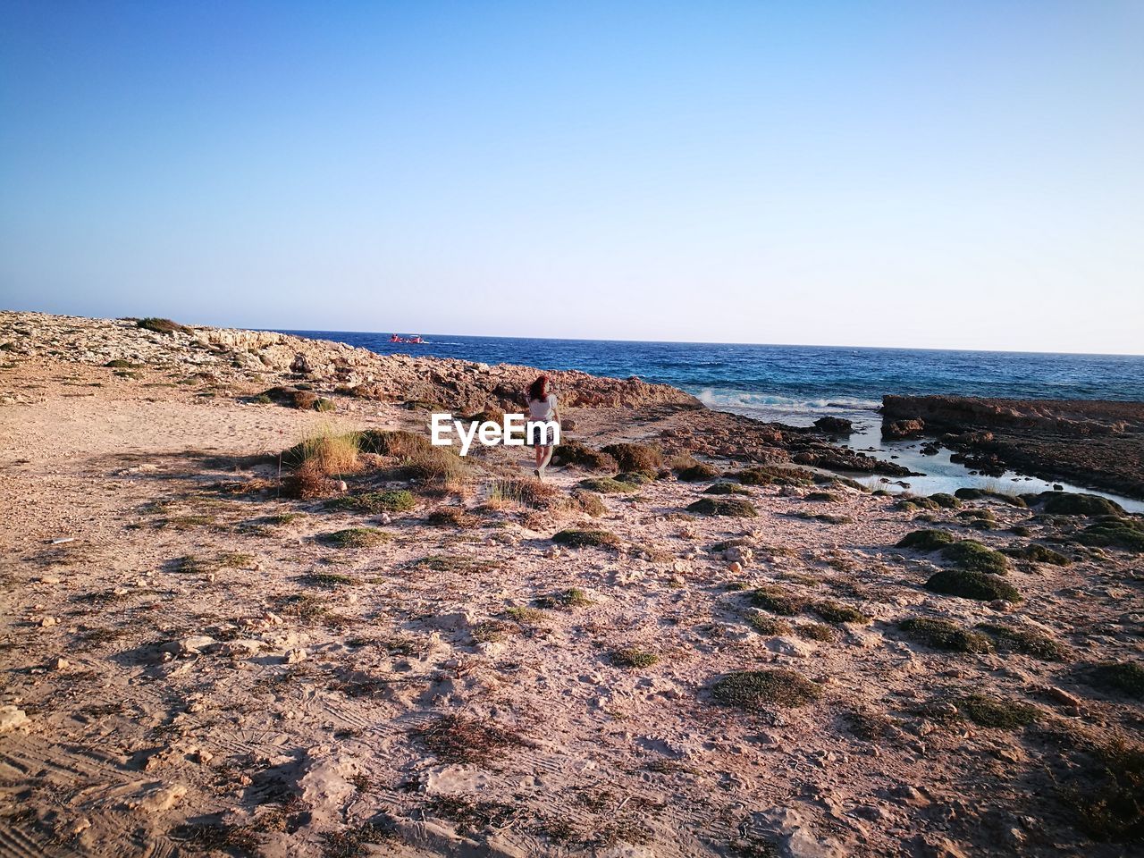 Women walking on coastline of sea against clear blue sky