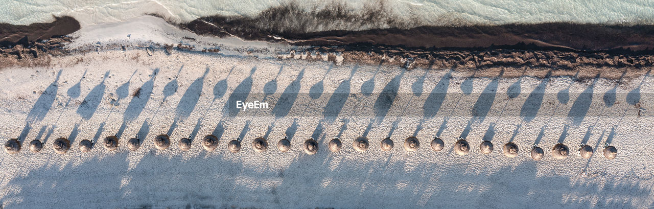 Lined up umbrellas seen from the air casting shadows over the white sand beach of es trenc, majorca
