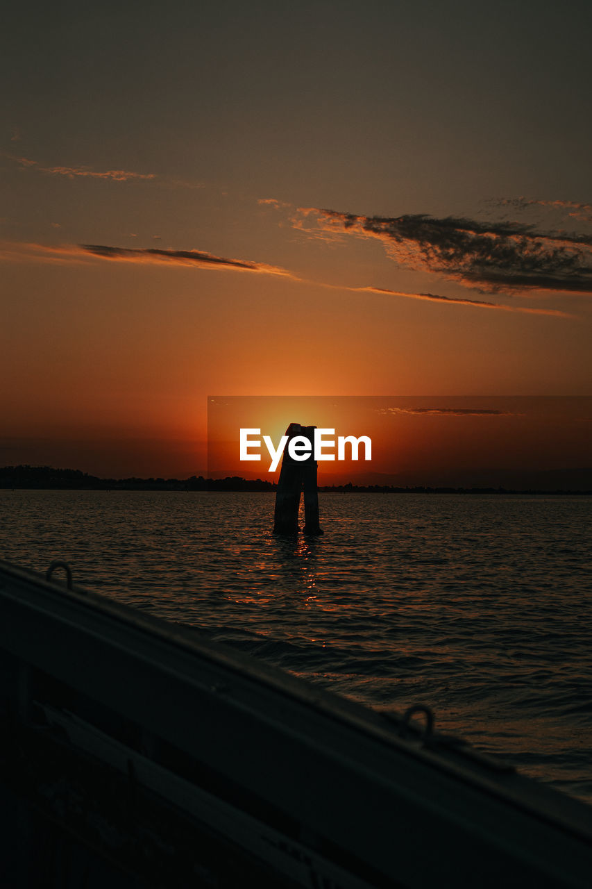 SILHOUETTE MAN STANDING ON SEA AGAINST SKY DURING SUNSET