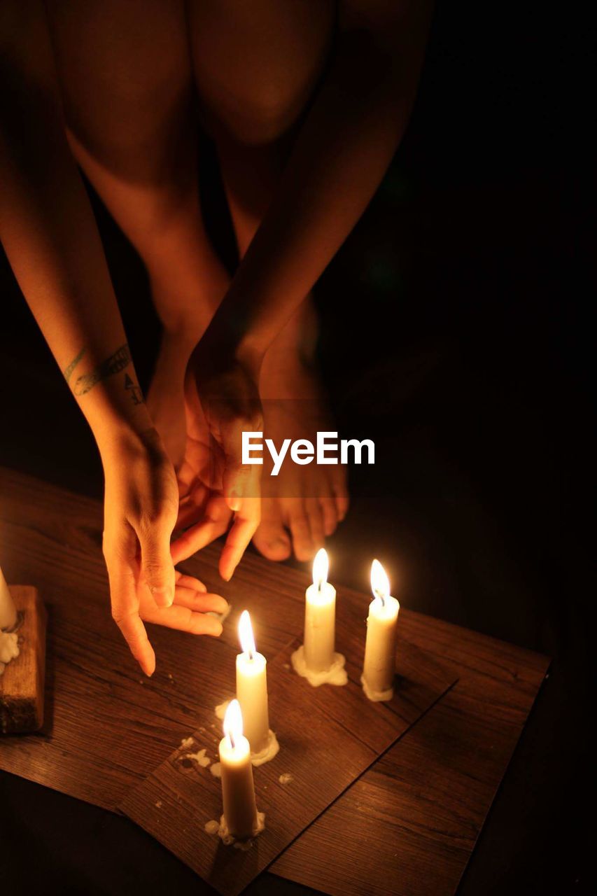 Close-up of woman bending by candles on table in darkroom