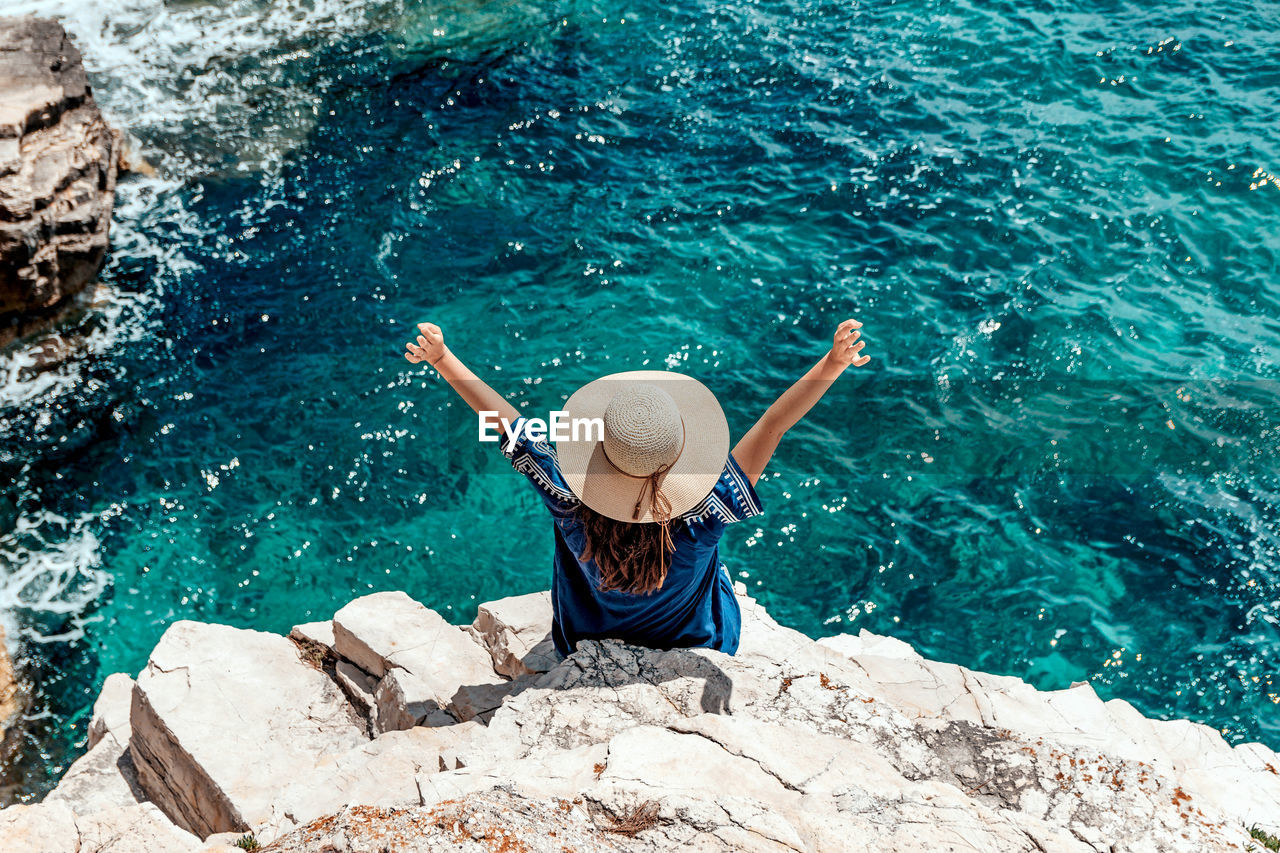 Young woman in summer outfit on cliff above sea.