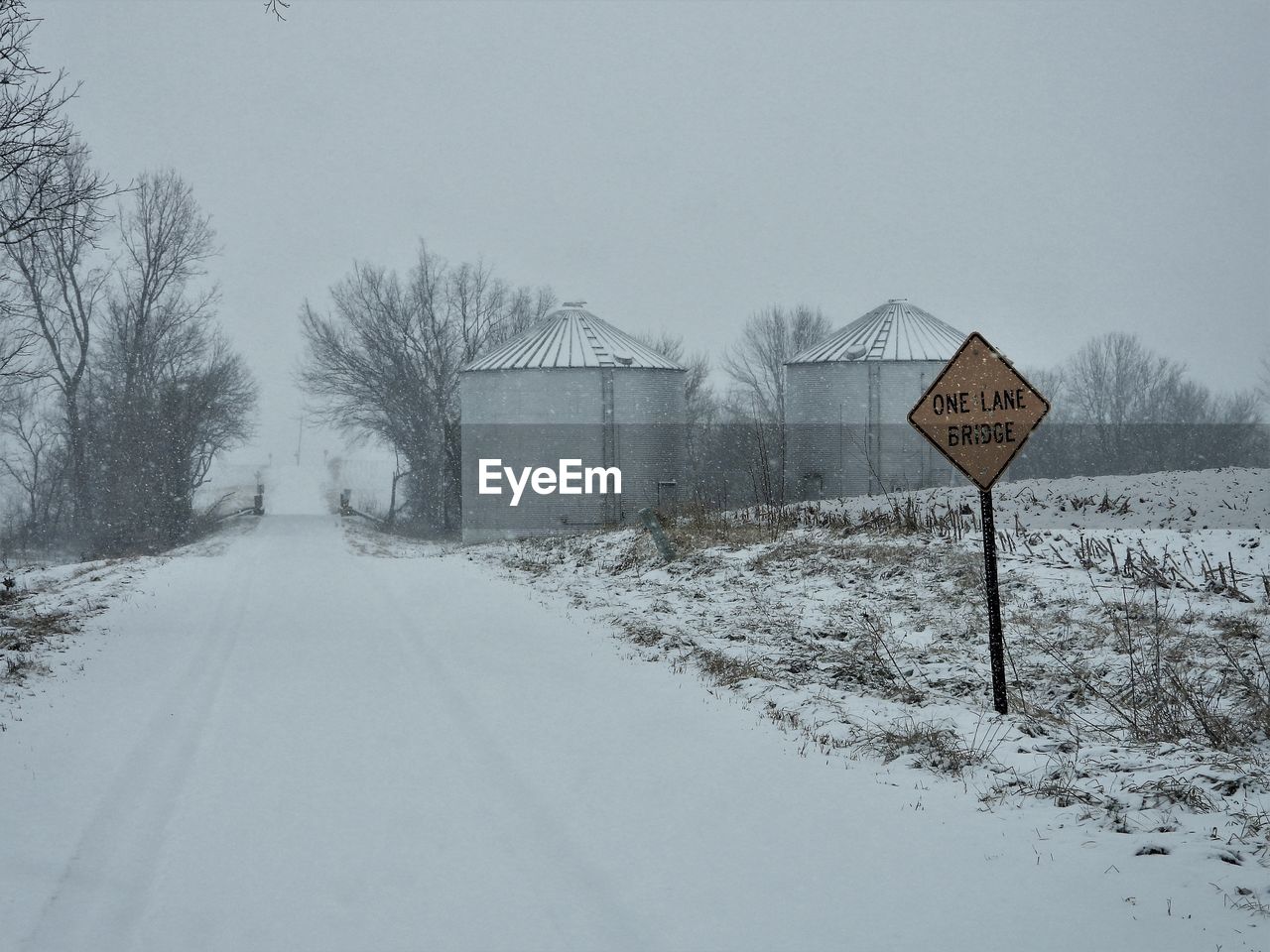 ROAD SIGN AMIDST SNOW COVERED FIELD AGAINST SKY