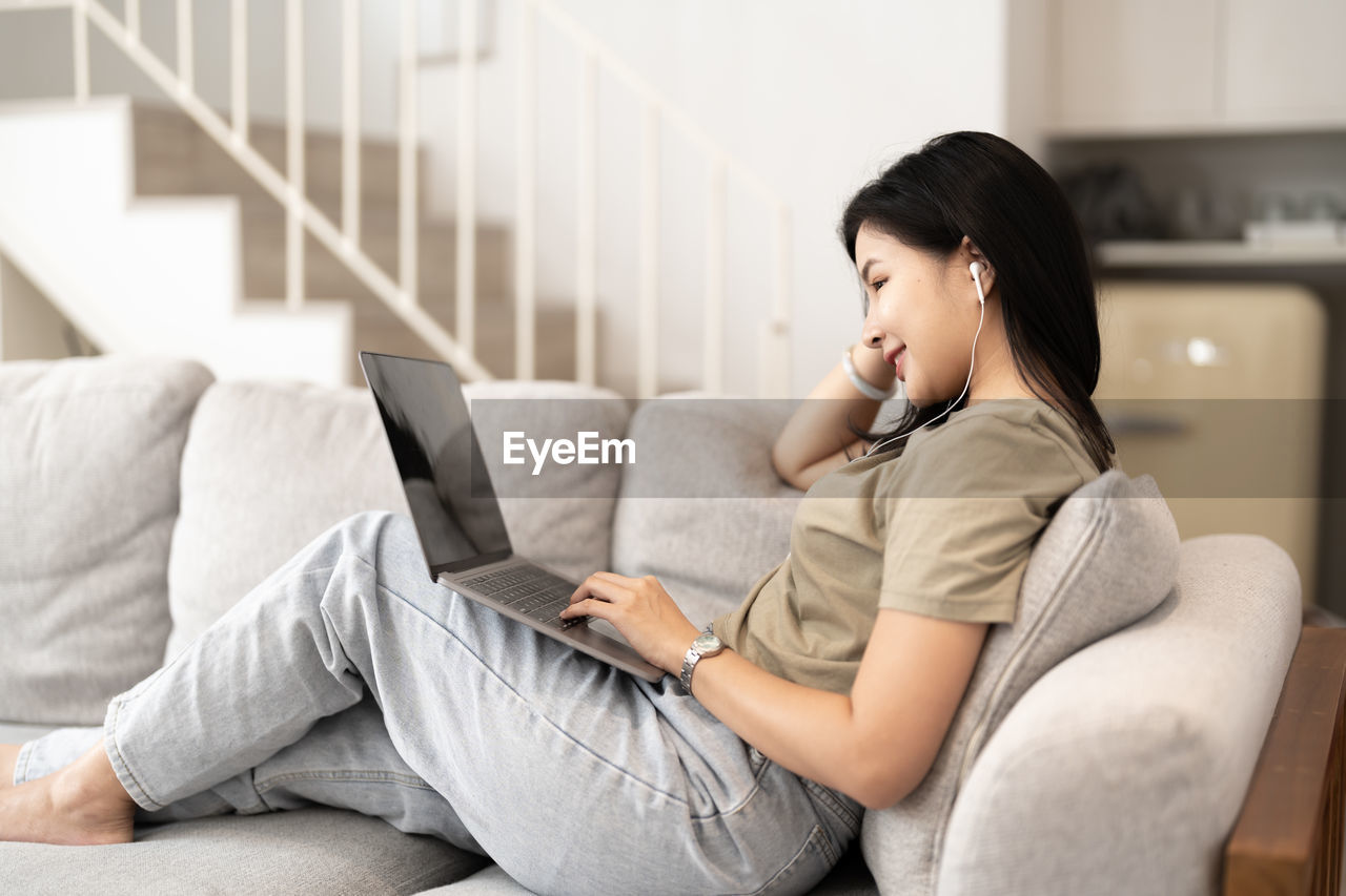 young woman using mobile phone while sitting on sofa at home