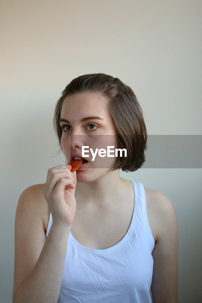 CLOSE-UP PORTRAIT OF YOUNG WOMAN EATING AGAINST GRAY BACKGROUND