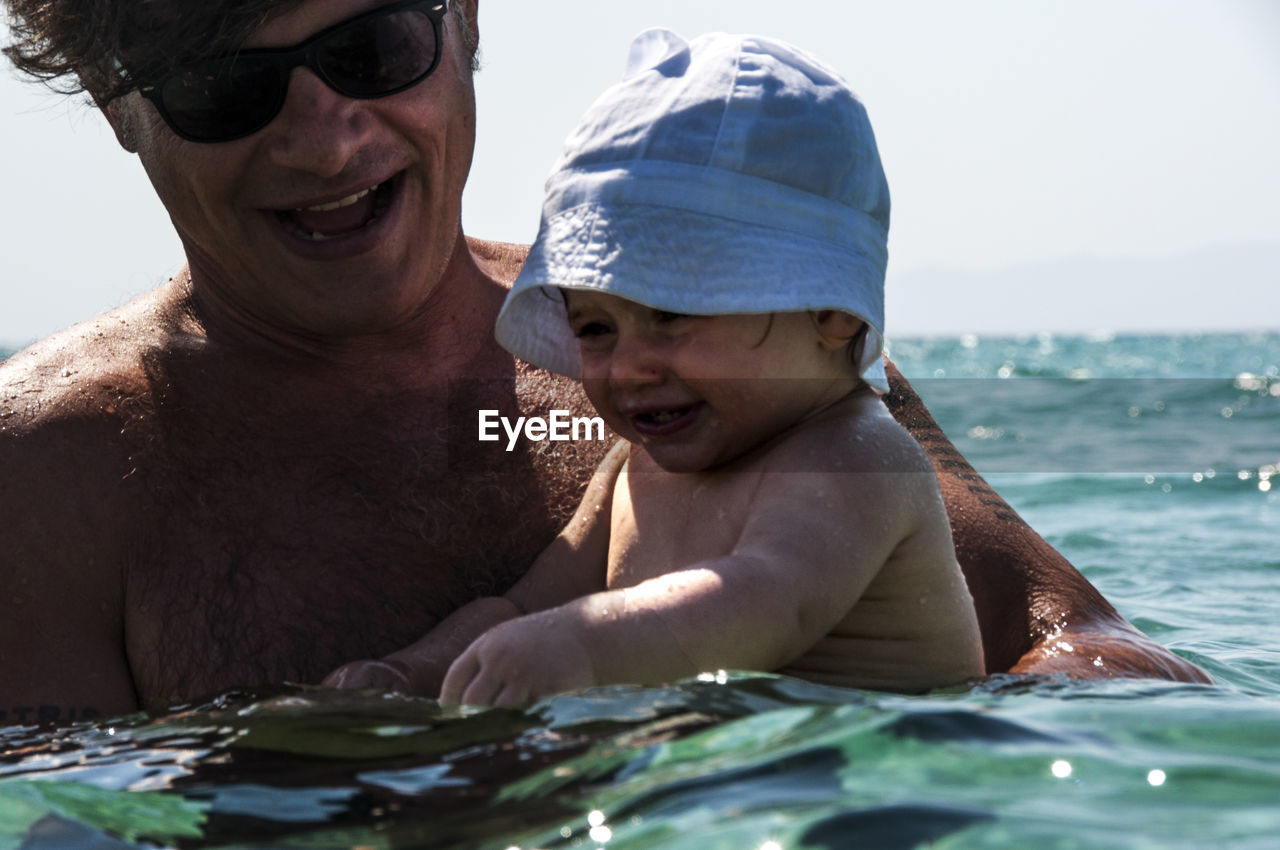 Close-up of father and daughter swimming in sea against sky