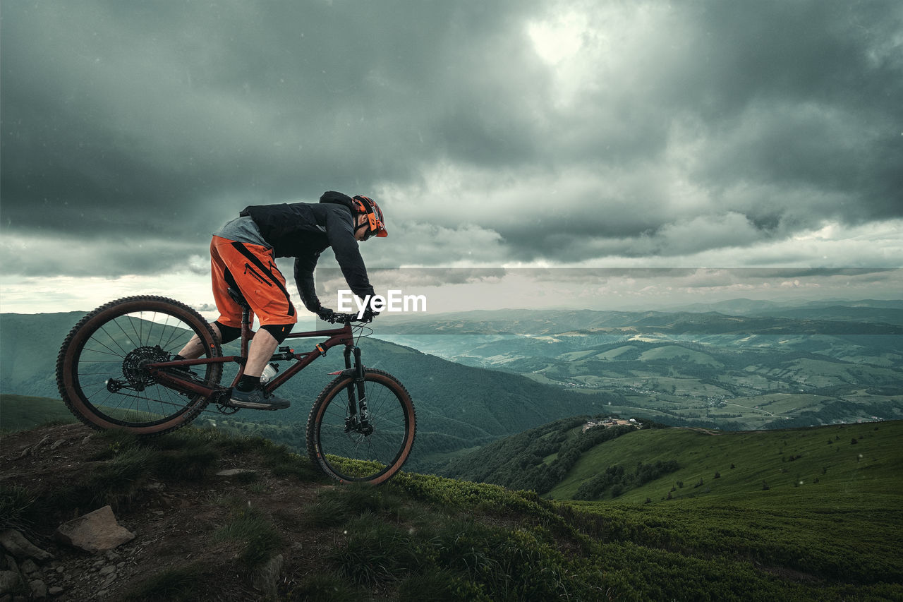 Man riding bicycle on mountain against sky