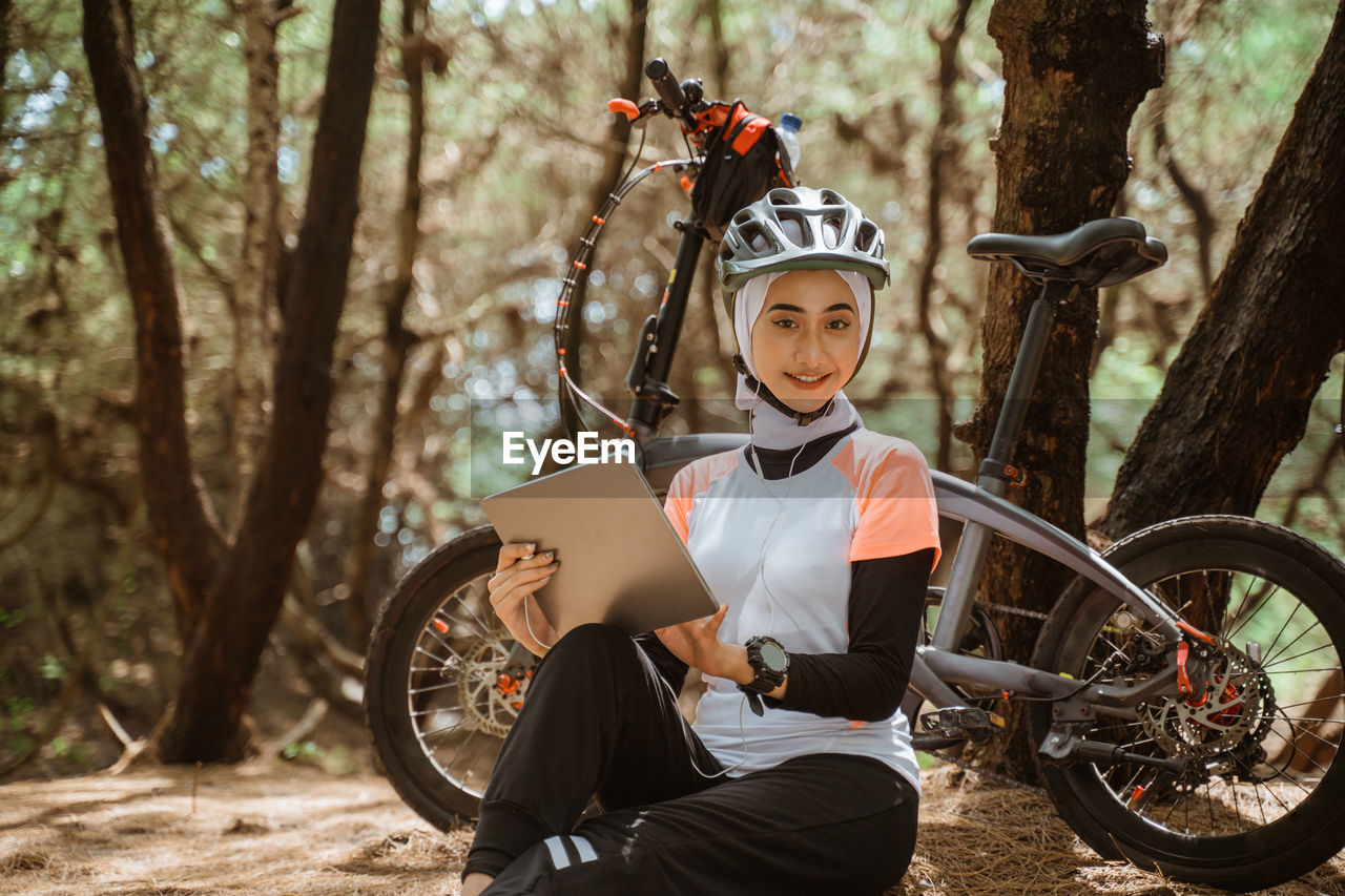 Portrait of smiling woman holding digital tablet sitting at park