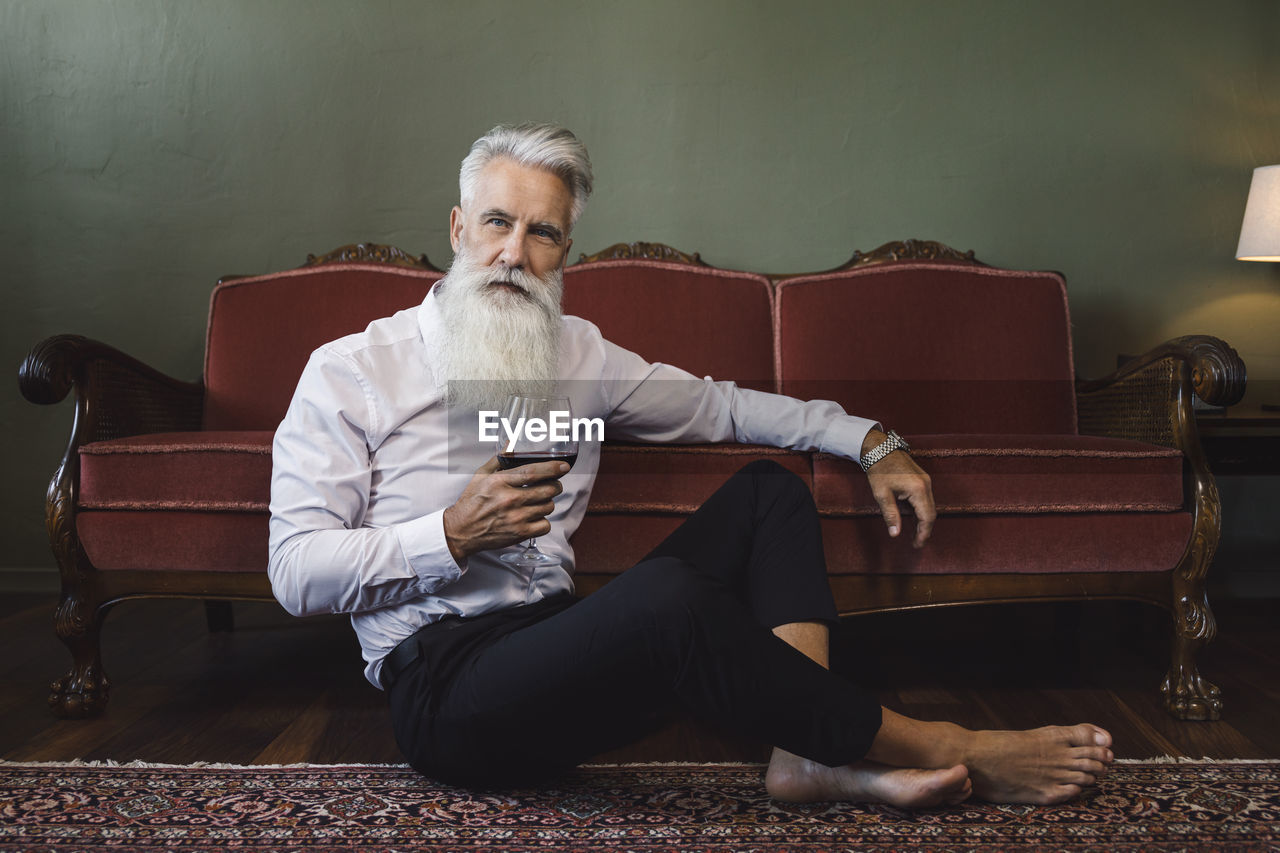 portrait of senior man using mobile phone while sitting on sofa at home