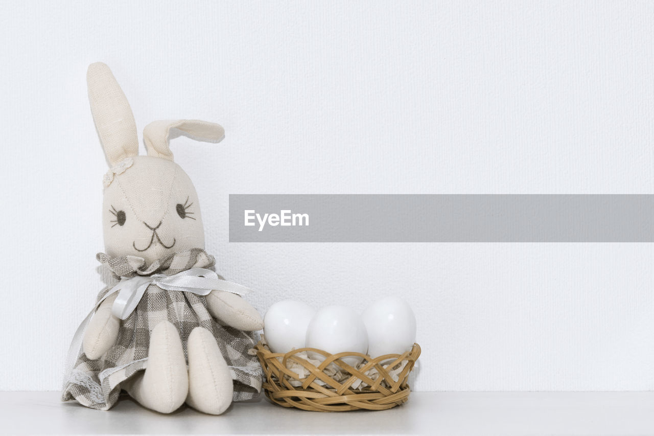 Easter composition with a soft rabbit toy and white eggs in a basket on a shelf in the room