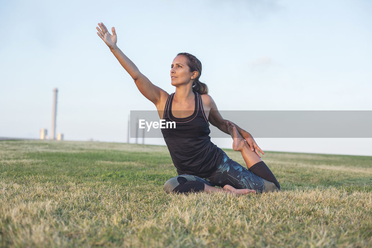 Mature woman exercising while sitting on field against sky