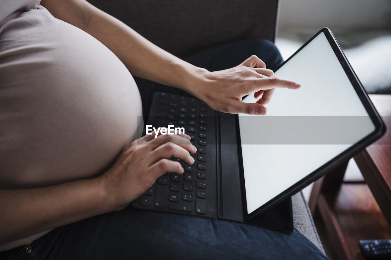 Pregnant woman using laptop while sitting on sofa in living room