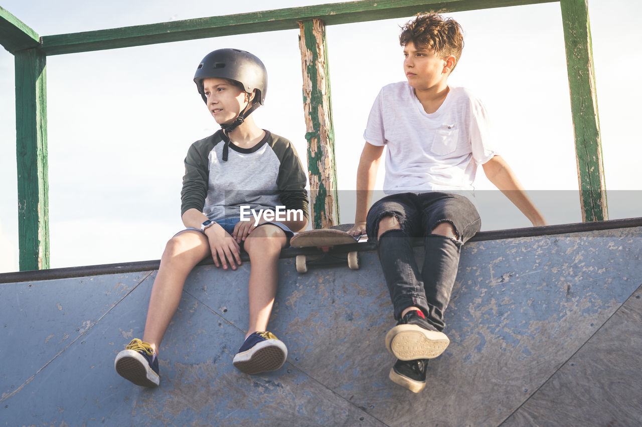 Low angle view of boys sitting on wall against sky