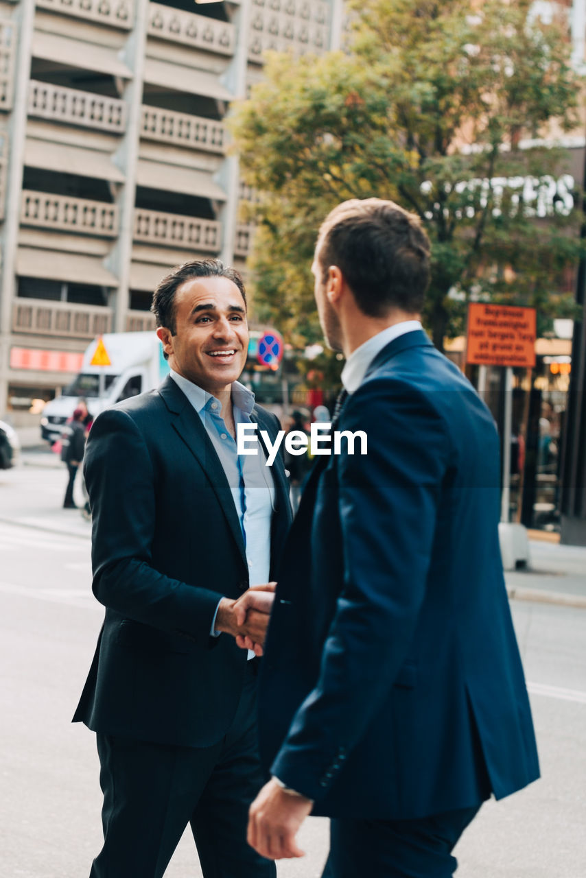 Smiling mature businessman greeting male colleague on street in city