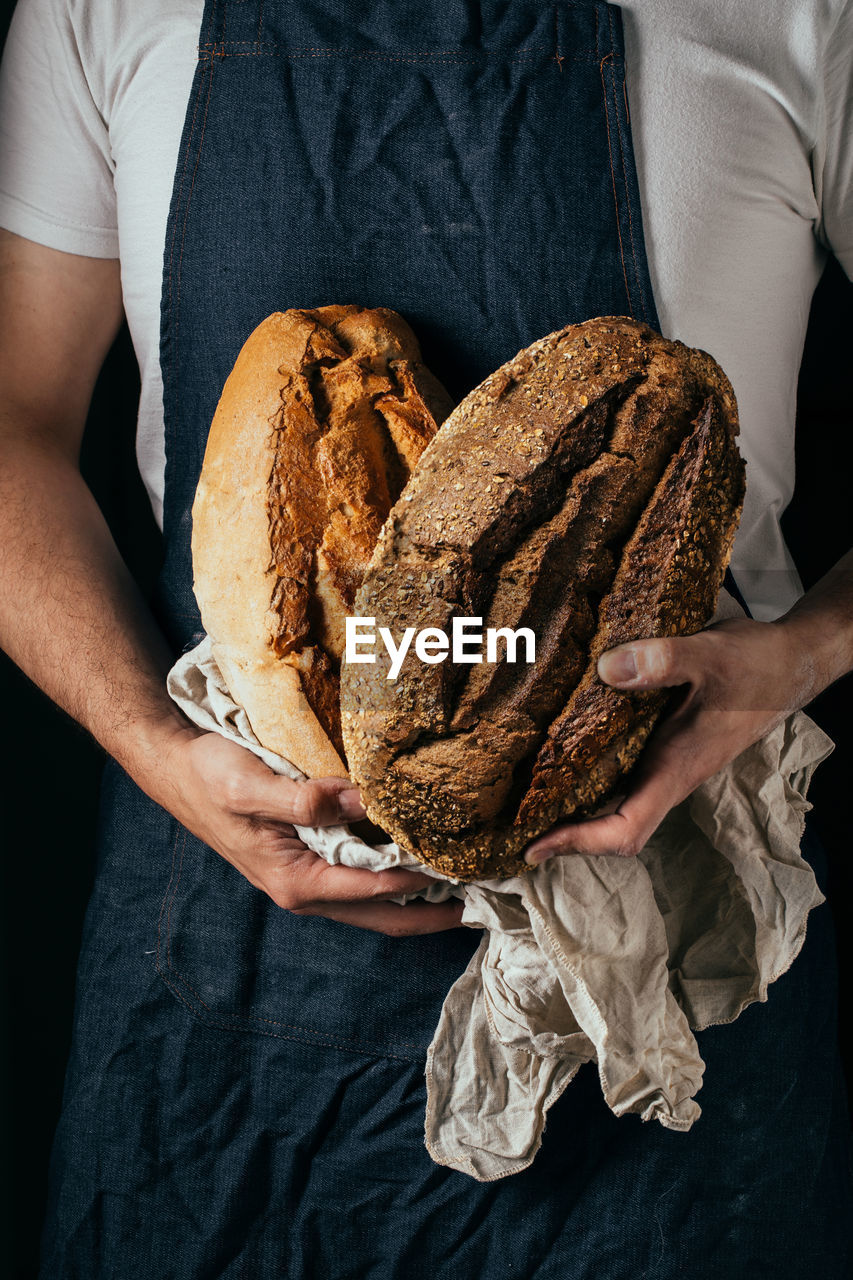 Crop unrecognizable male baker in apron demonstrating loaf of fresh crispy breads in kitchen