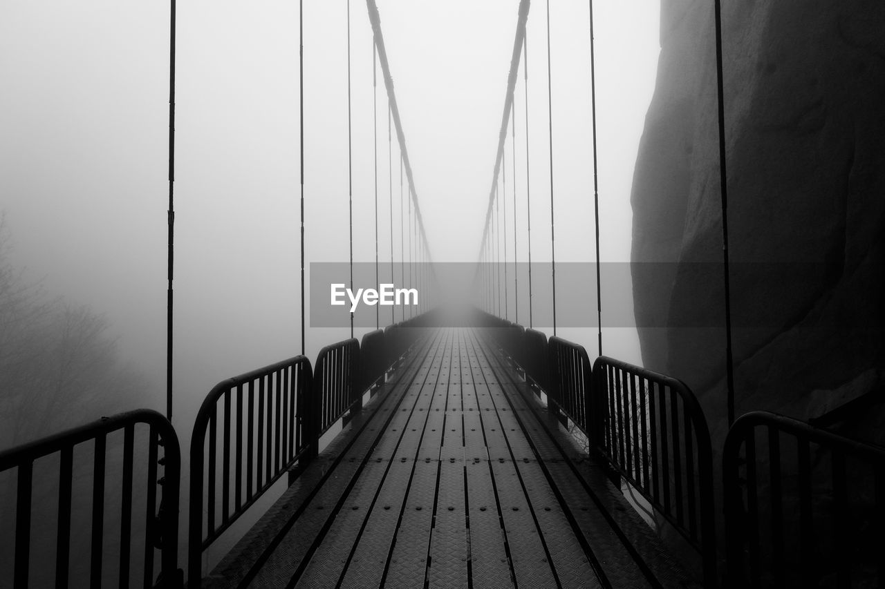 Empty footbridge in fog against sky